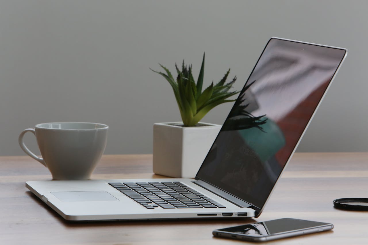 who-we-are-03 Minimalist home office desk with laptop, smartphone, and plant for a modern work environment.